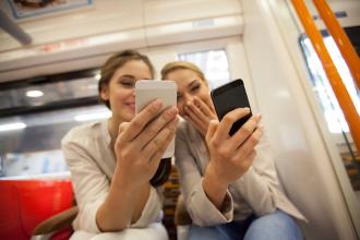 
		Zwei junge Frauen sind in der U-Bahn und schauen in ihre Smartphones
	
